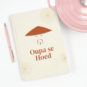 Cream notebook with Oupa se Hoed logo and text on the cover, next to a pencil and pink cup.